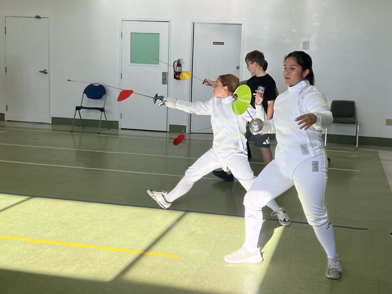 Two fencers extending into a lunge during a drill
