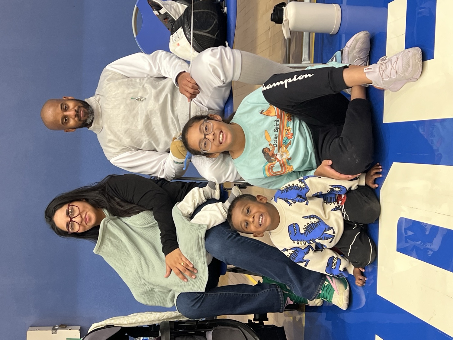 A family with two kids sitting together at a fencing meet