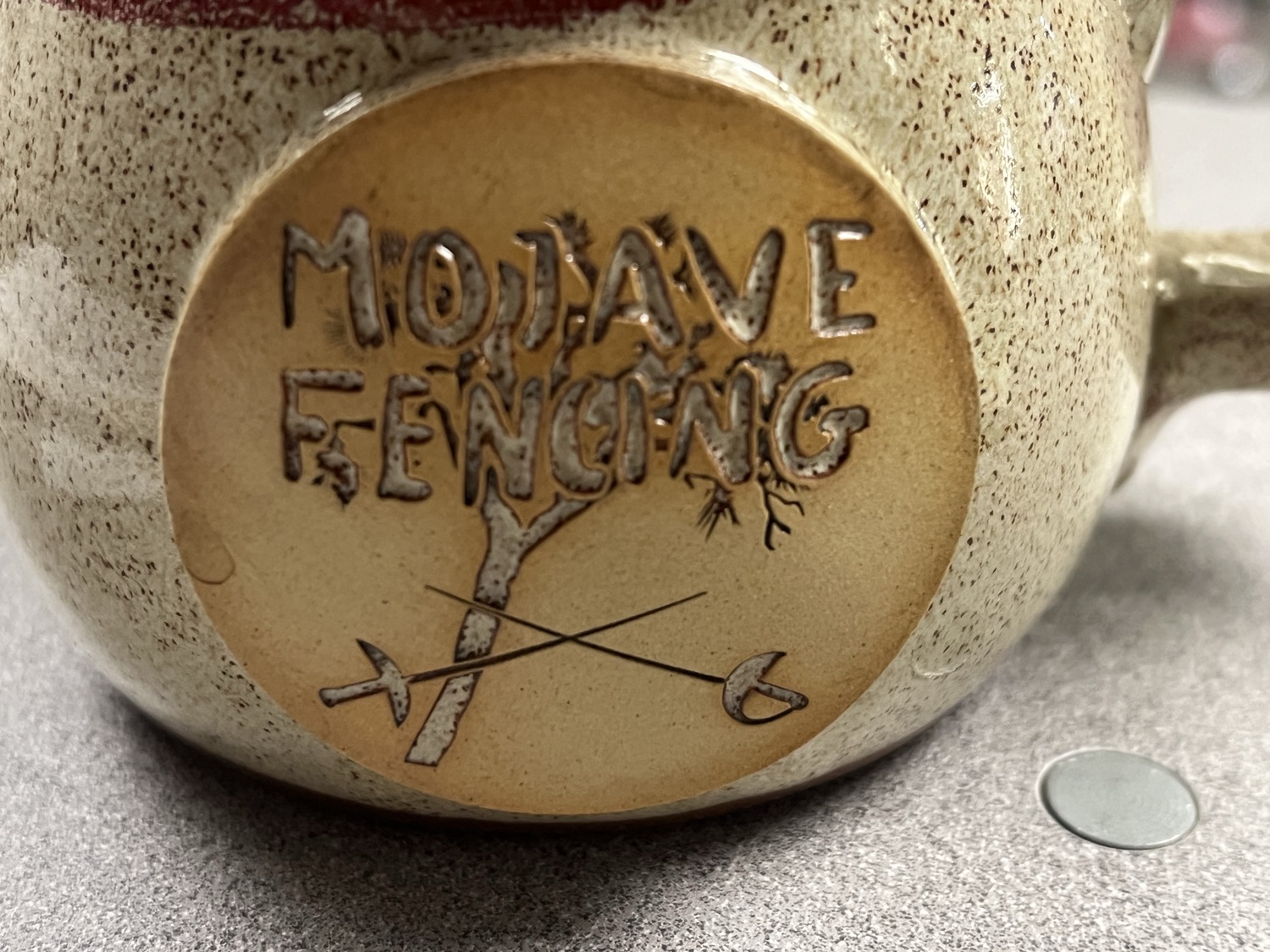 Close-up of the hand-carved Mojave Fencing medallion with crossed blades on the mug